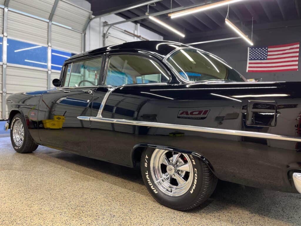 a classic black car displayed in a garage with an american flag in the background.