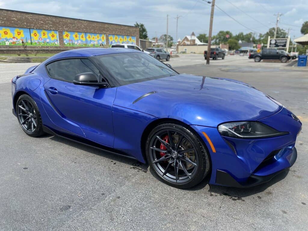 a blue sports car parked on an asphalt surface with murals in the background.