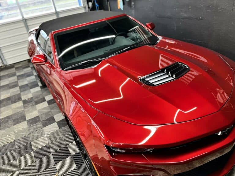 a red convertible sports car with a black soft top is parked in a garage with checkered flooring.