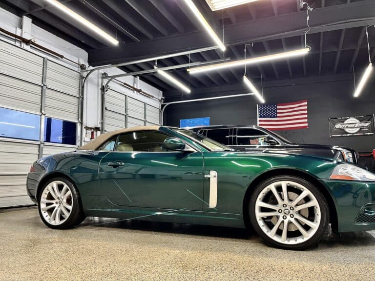 a dark green convertible car is parked indoors in a garage with an american flag on the wall.