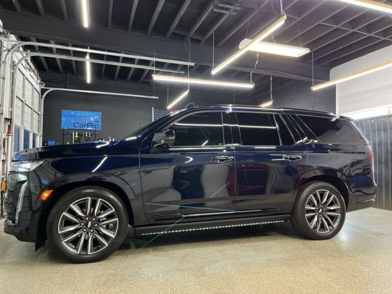 a black suv parked inside a well lit automotive workshop with reflective floors and various garage equipment visible in the background.