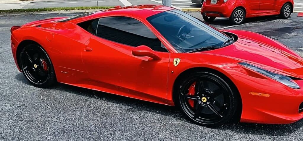 a red ferrari sports car is parked on a pavement. another red car is visible in the background.