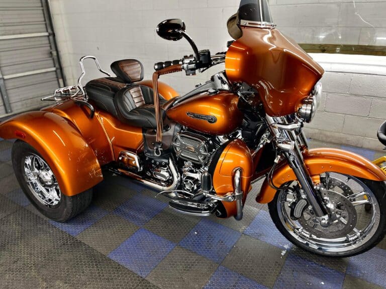 a custom orange trike motorcycle with chrome accents and leather seats, parked indoors on a checkered floor.