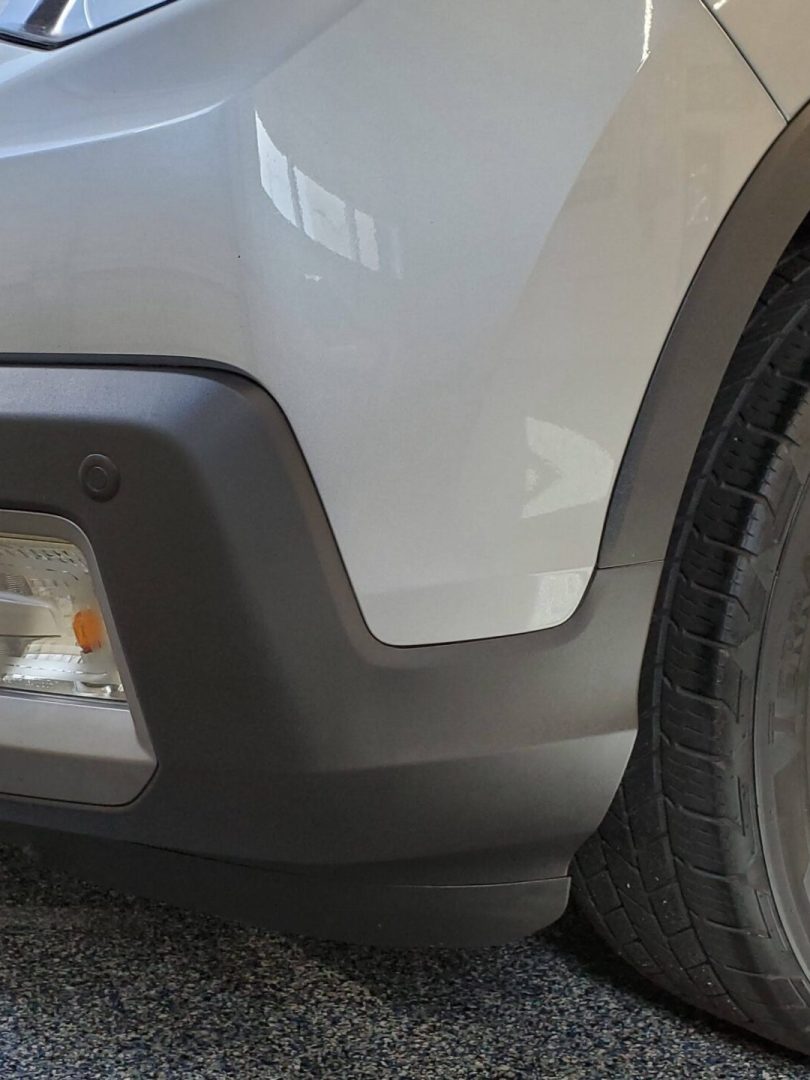 close up of the front right corner of a silver suv, showing the bumper, headlight, fog light, and alloy wheel on a speckled garage floor.