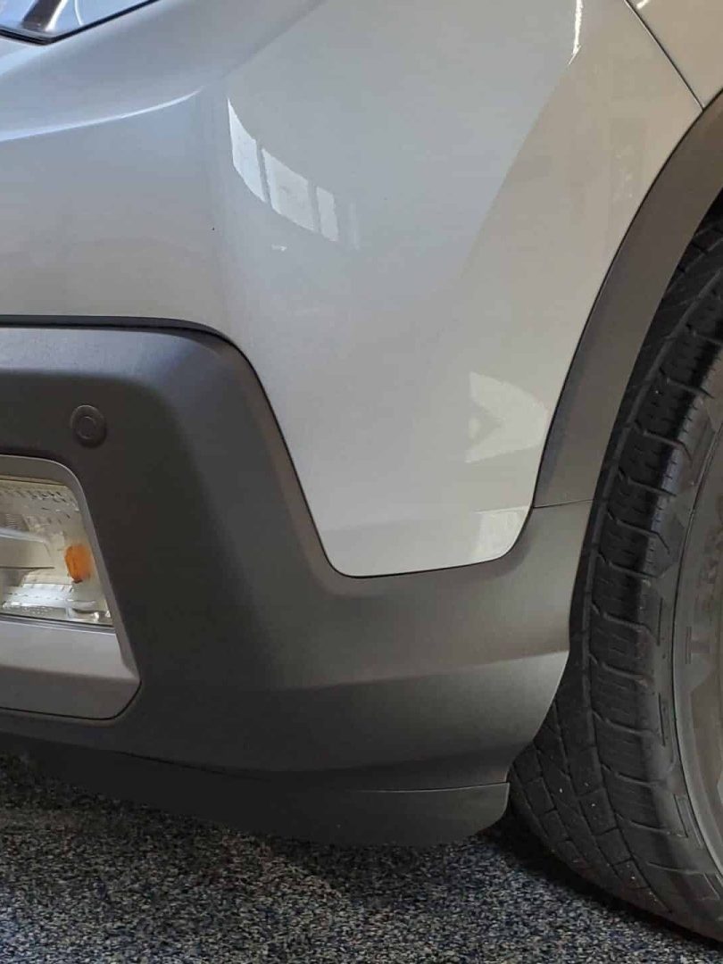 close up of the front right corner of a silver suv, showing the bumper, headlight, fog light, and alloy wheel on a speckled garage floor.