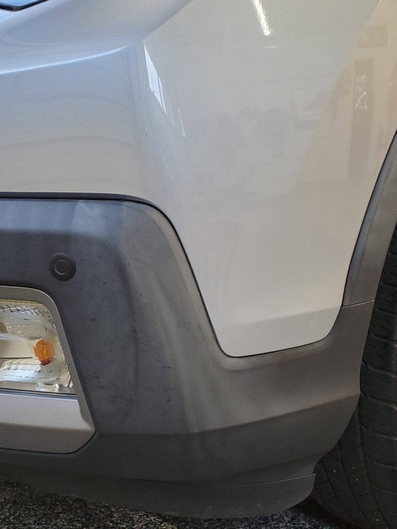 close up of the front right corner of a silver suv, showing the headlight, fog light, bumper, and tire on a speckled garage floor.