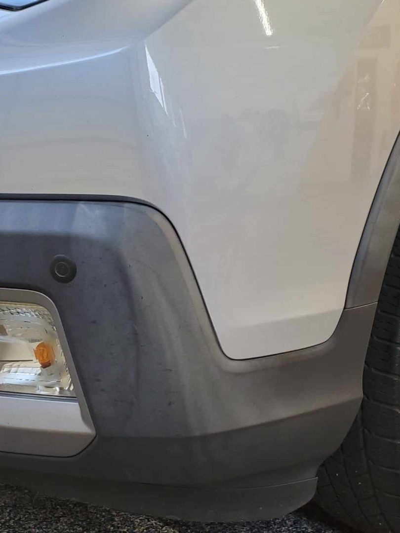 close up of the front right corner of a silver suv, showing the headlight, fog light, bumper, and tire on a speckled garage floor.